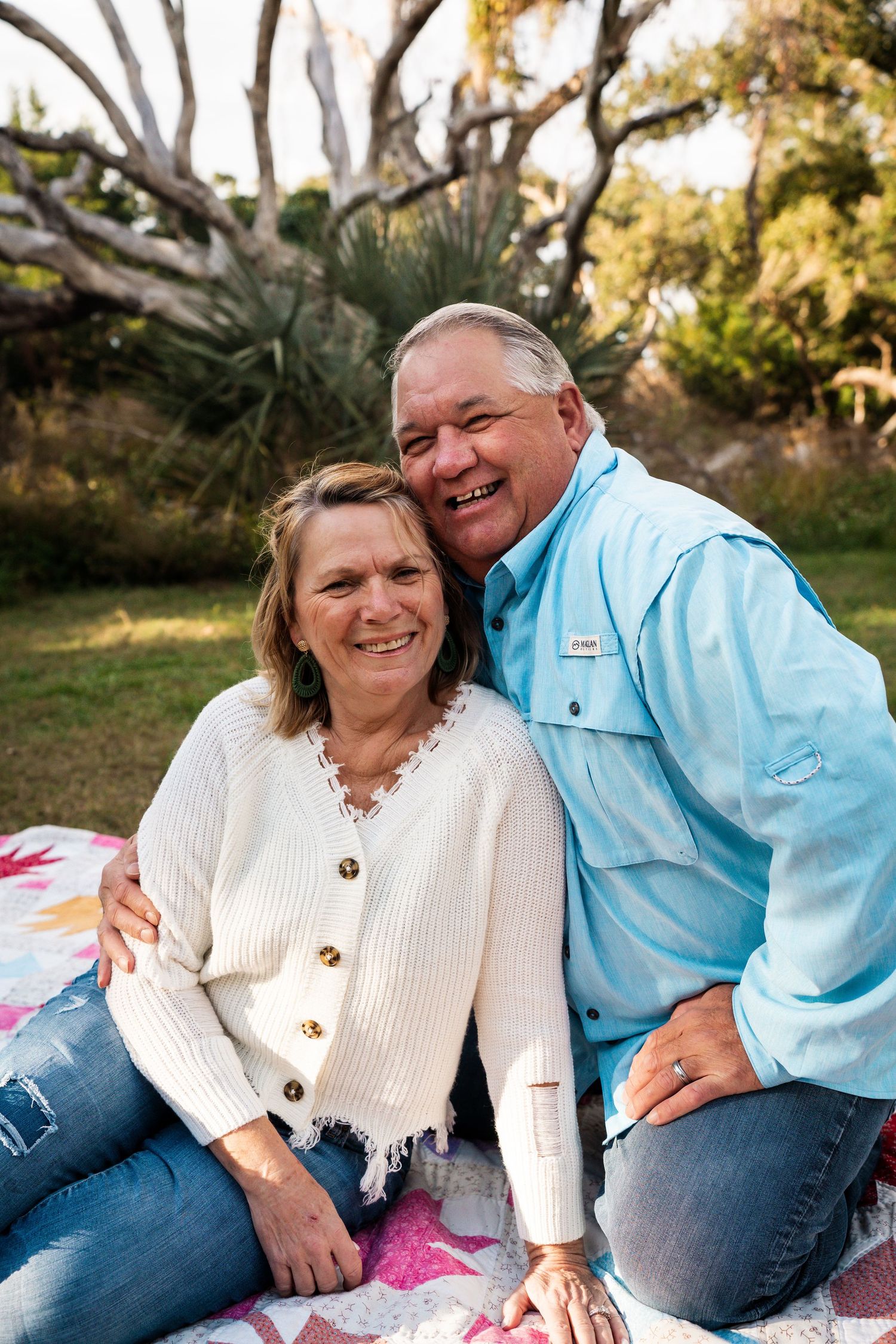Couple sitting together on a picnic blanket outdoors wearing casual clothing and smiling.