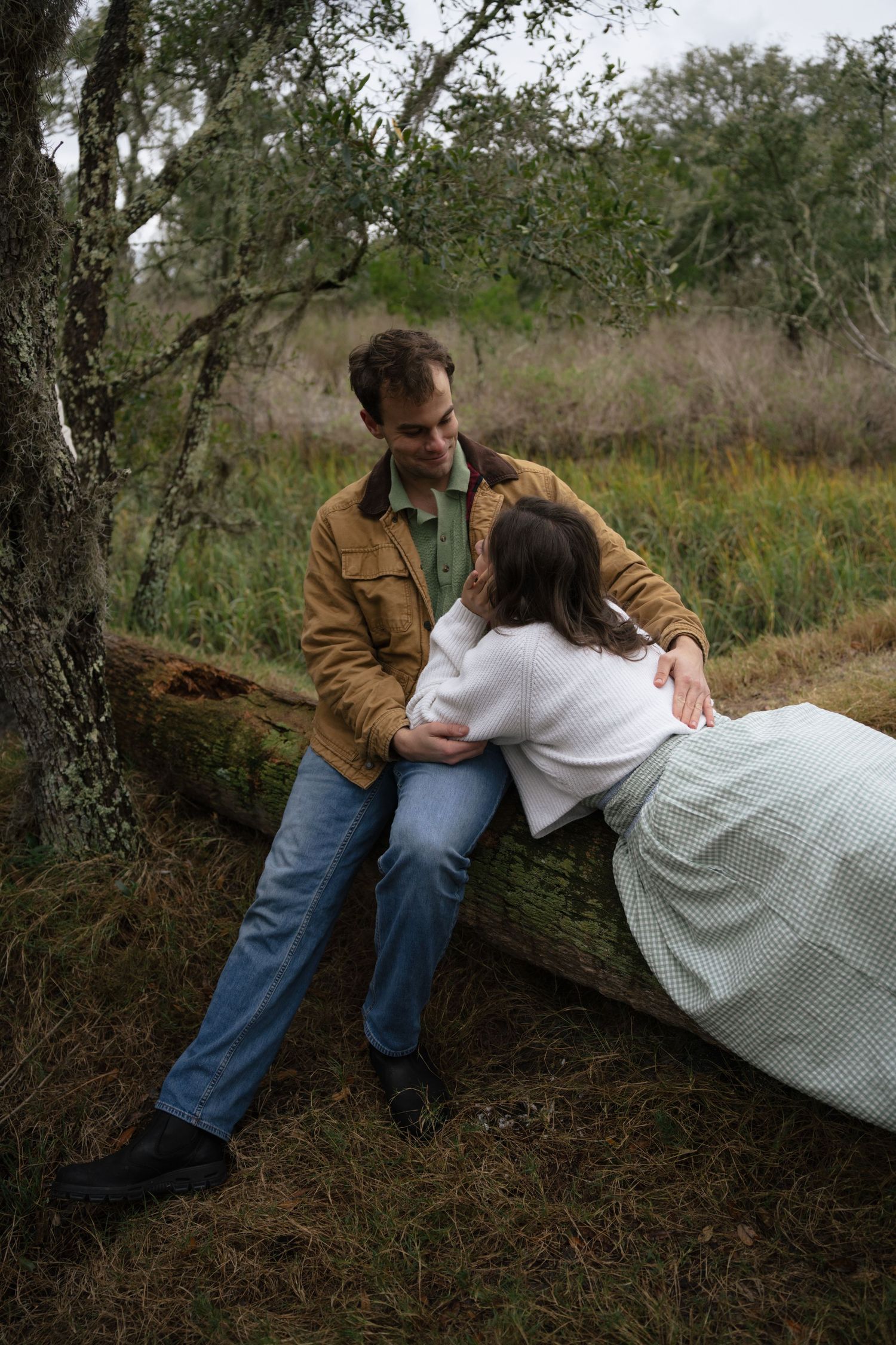 Two people rest together on a fallen tree trunk in a natural wooded setting.