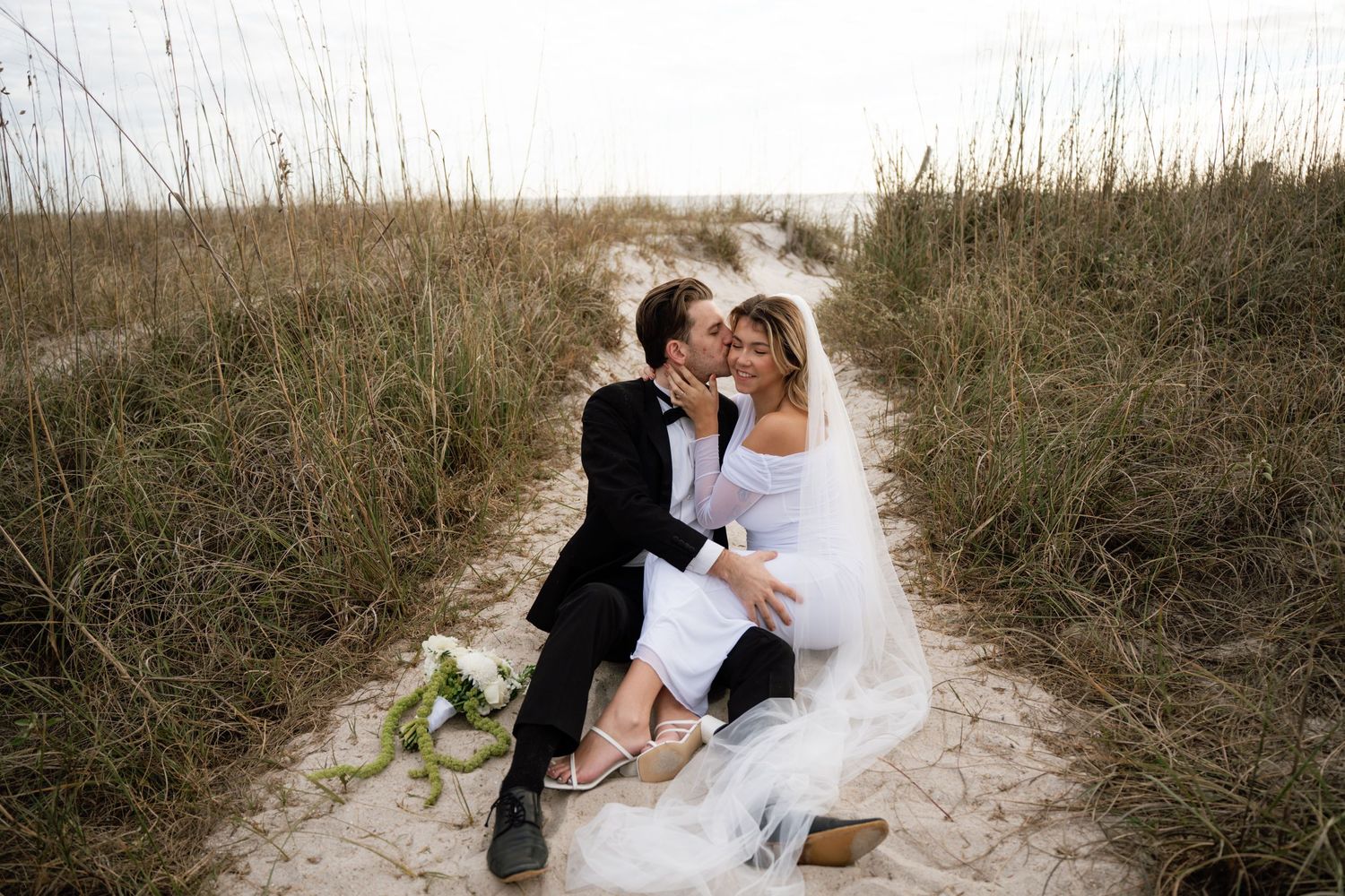 A romantic beach wedding photoshoot sequence showing tender moments between newlyweds on sandy dunes at sunset.