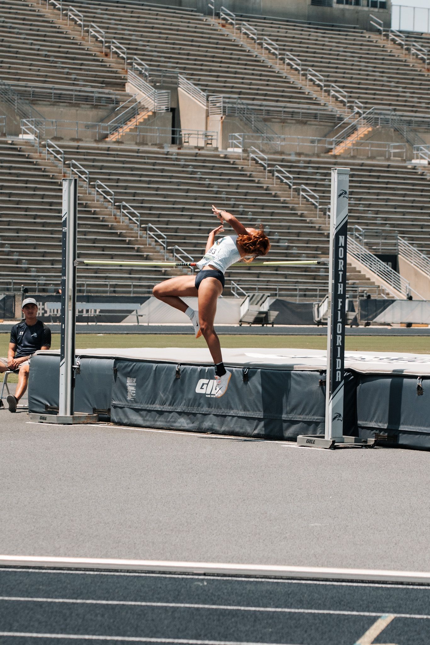Female athlete performing high jump at a track and field stadium, clearing the bar with an arched back technique.