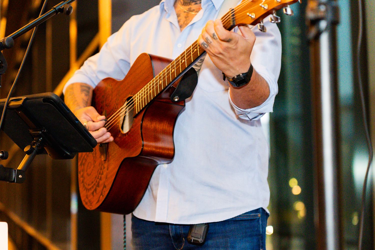 Man in white shirt playing acoustic guitar on stage with music stand visible in background.