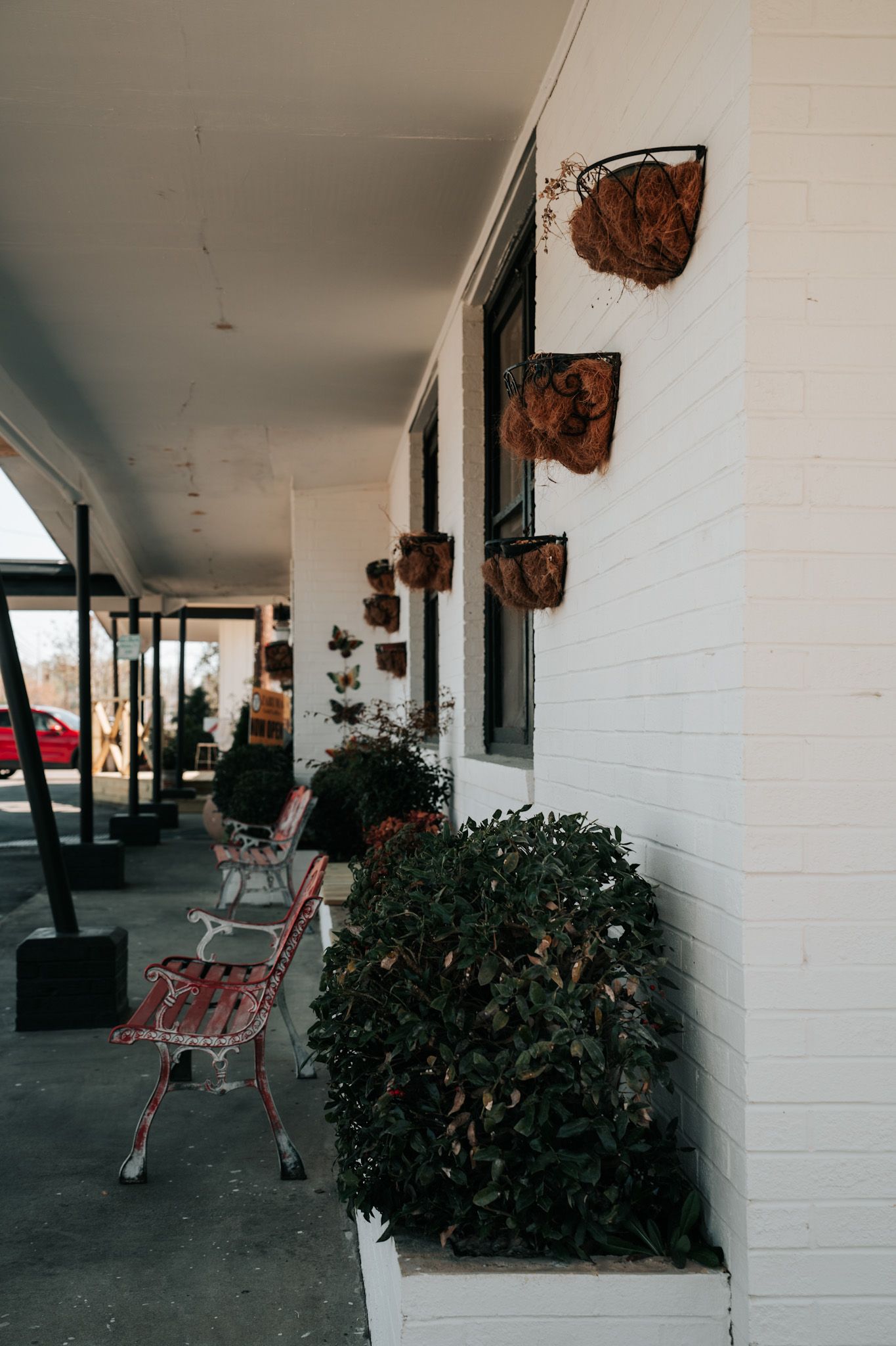 Vintage industrial corridor with red chairs, rustic wall decor, and potted plants along a white brick wall.