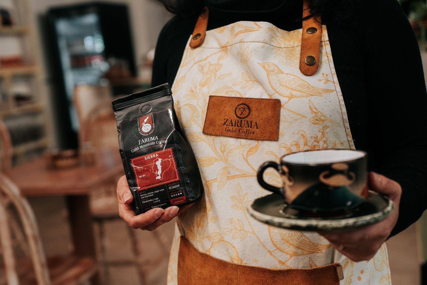 Coffee lover displays a bag of Alma Coffee and dark teacup while wearing a vintage-style cream canvas apron.