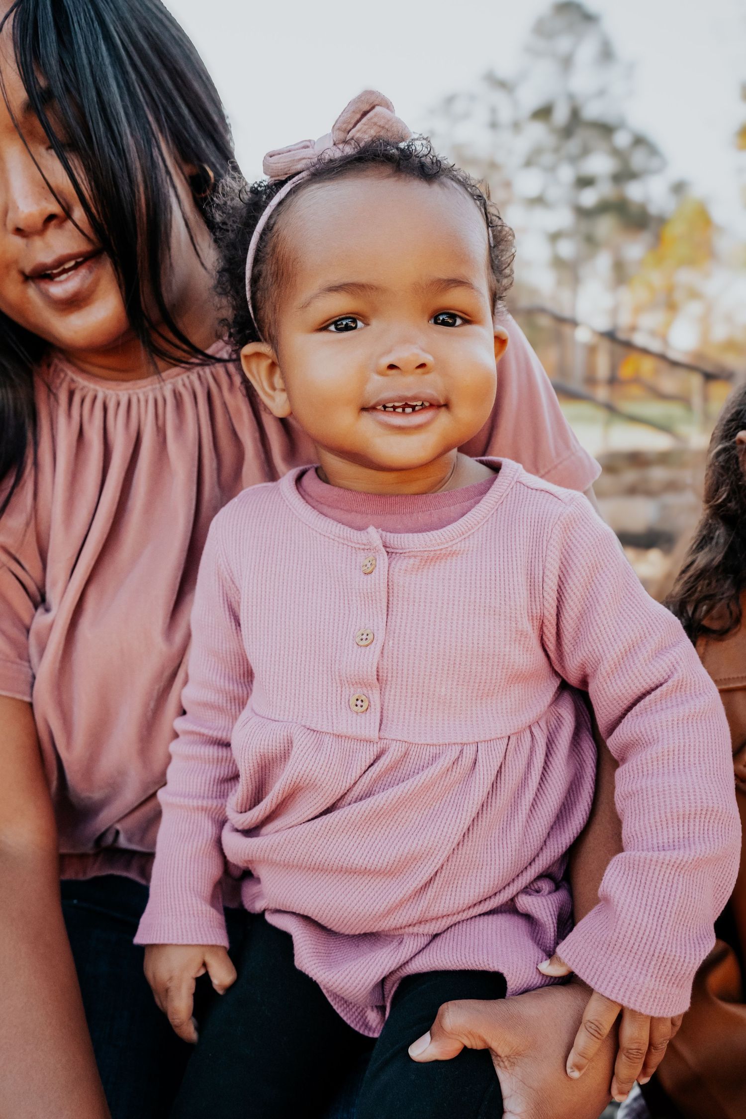 Young child in pink sweater dress smiling brightly outdoors.