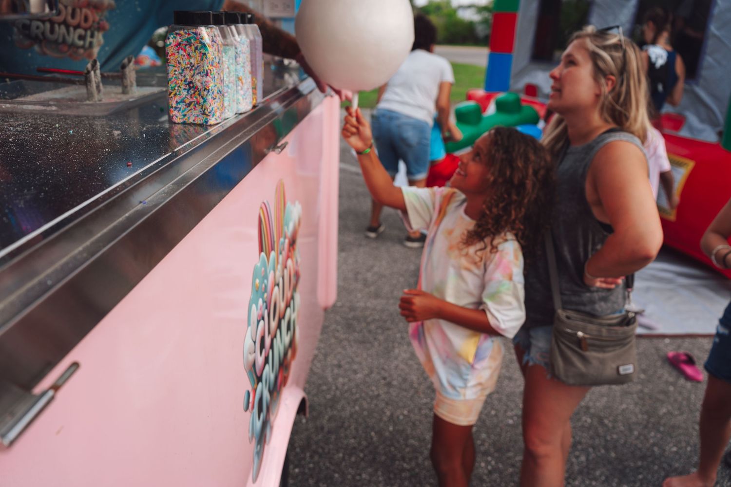 Woman and child at a pink cotton candy food truck at an outdoor festival event.