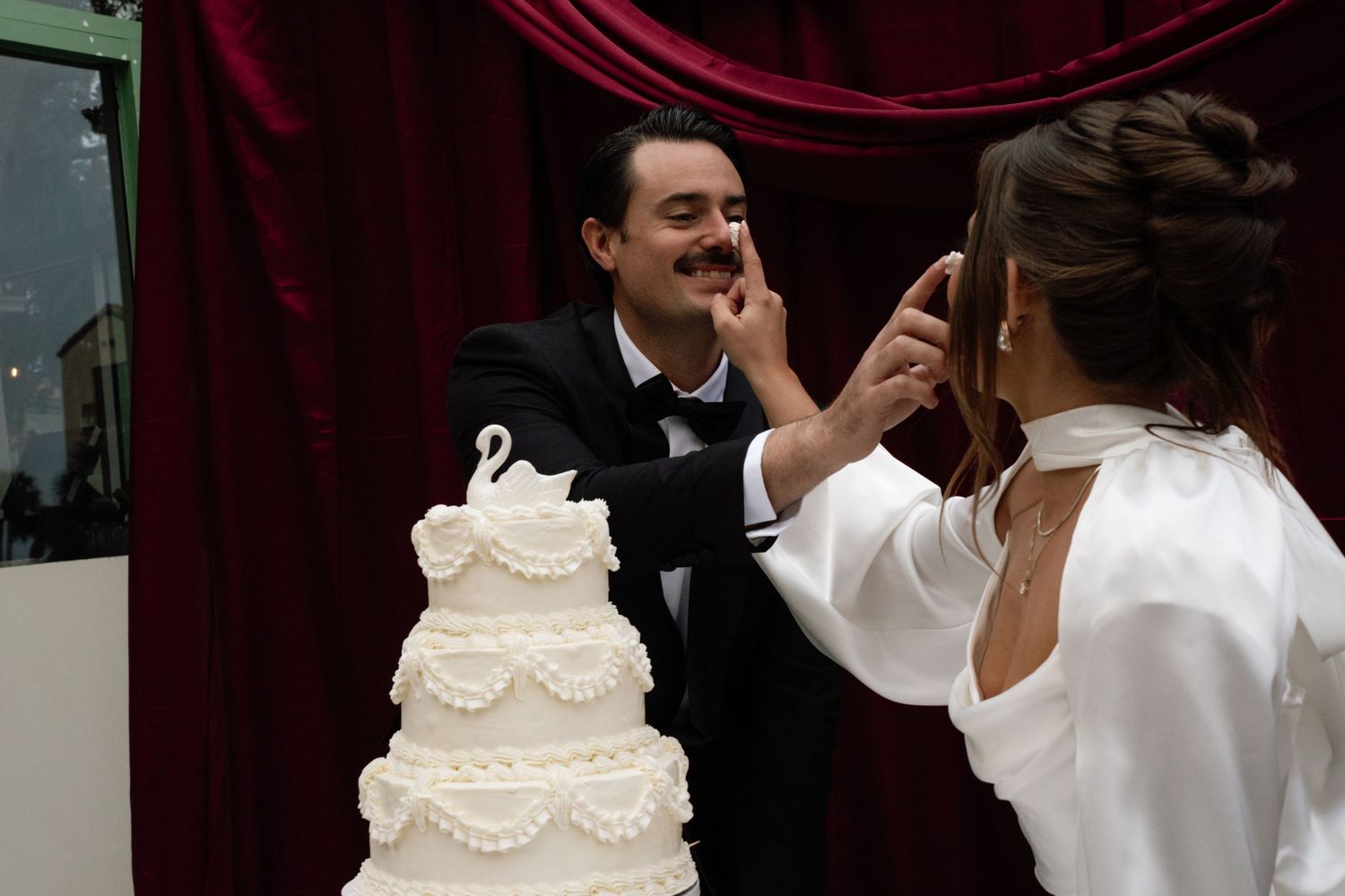 A bride and groom perform a cake cutting ceremony at their wedding reception with a traditional white tiered cake.