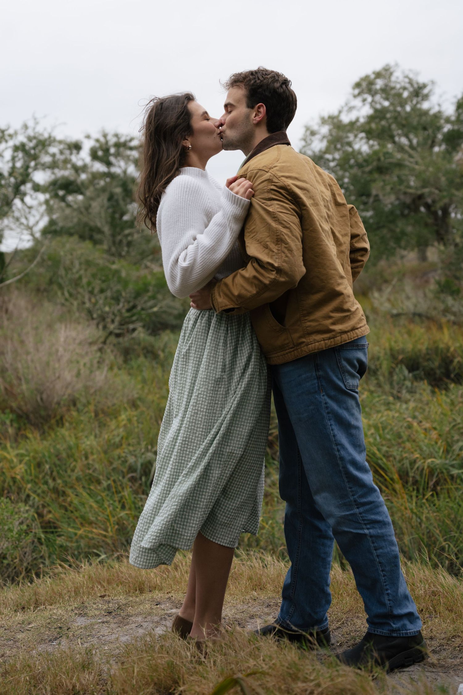Two children share a sweet moment in a field wearing casual clothing.