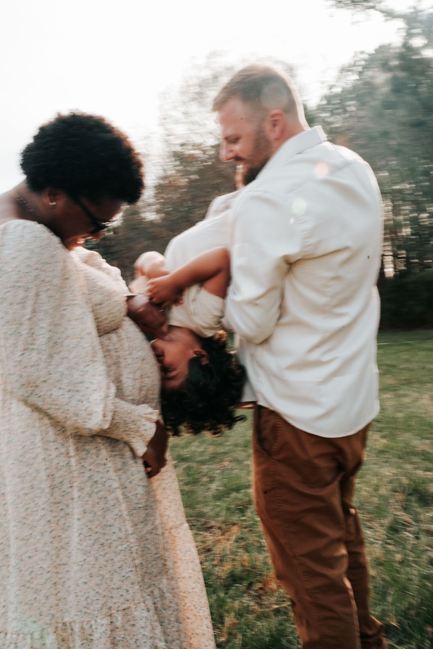 A couple in casual attire share a tender moment with their baby outdoors during golden hour.