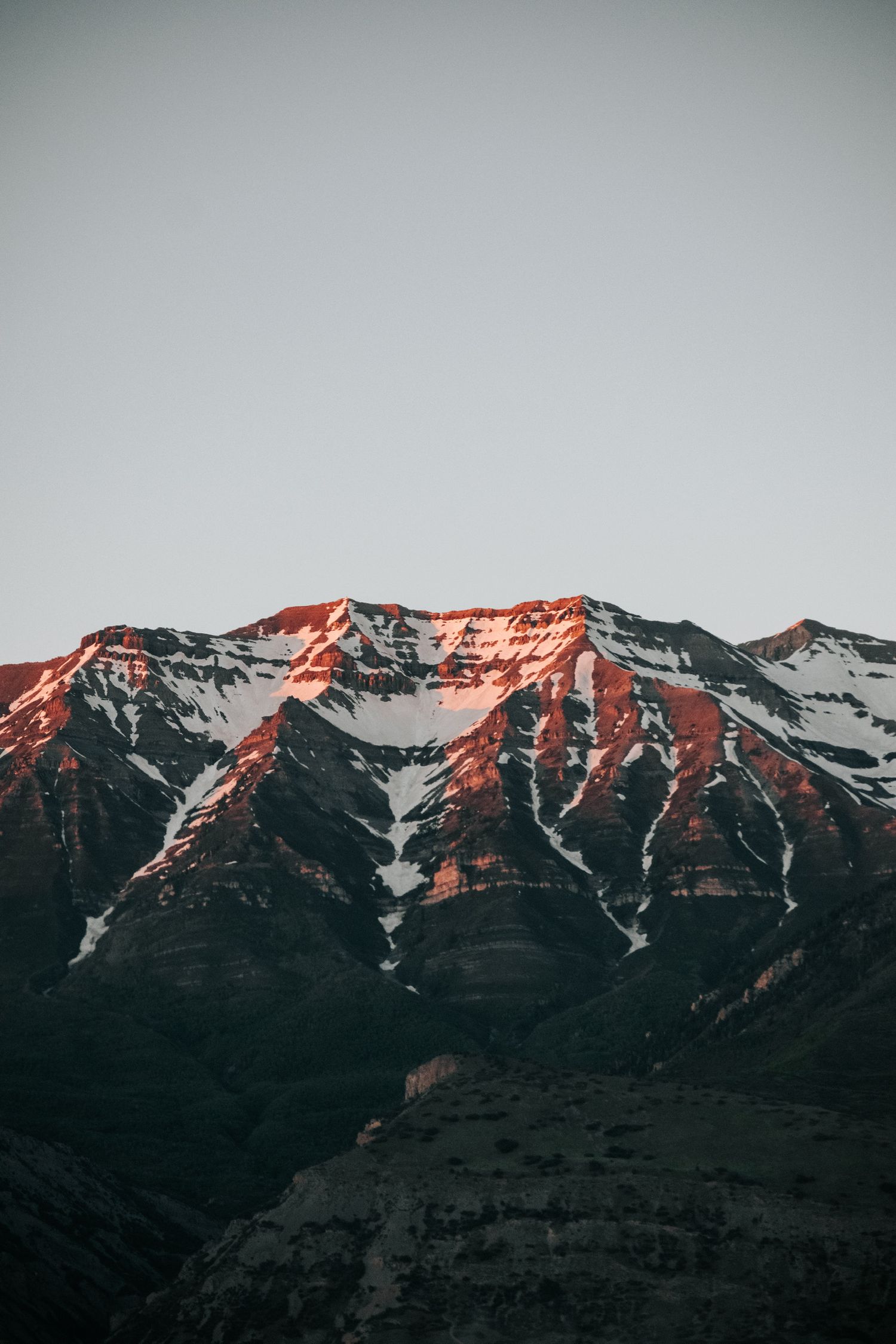 Snow-capped mountain peaks illuminated by warm sunset light against a dark moody sky.