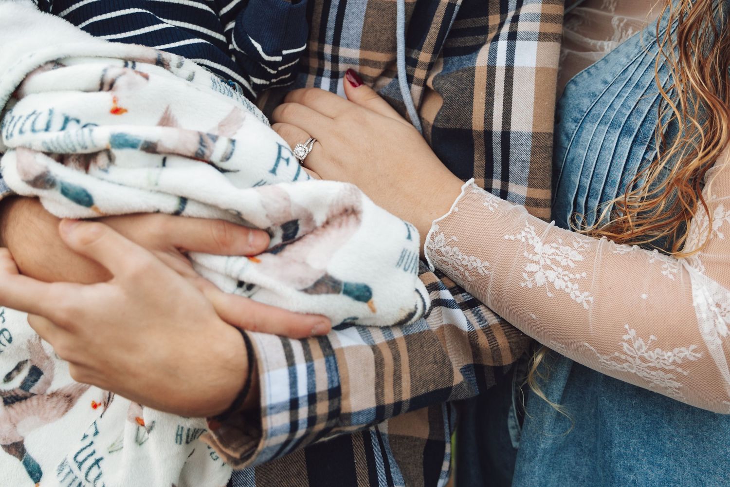 A small white and grey kitten being held in someone's arms wrapped in a plaid blanket.