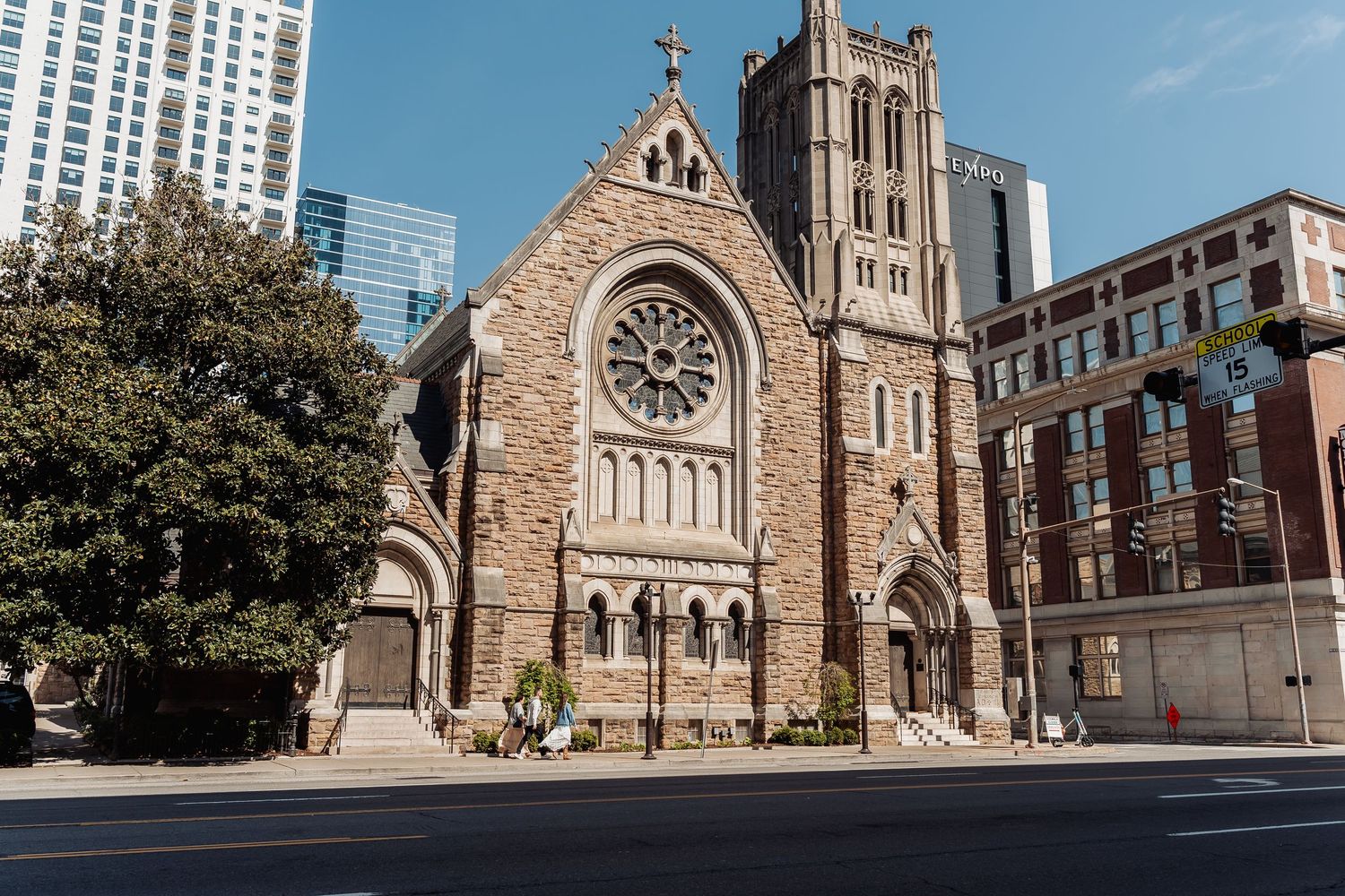 Historic Gothic Revival church with stone facade and tall spires stands prominently on a city street corner.