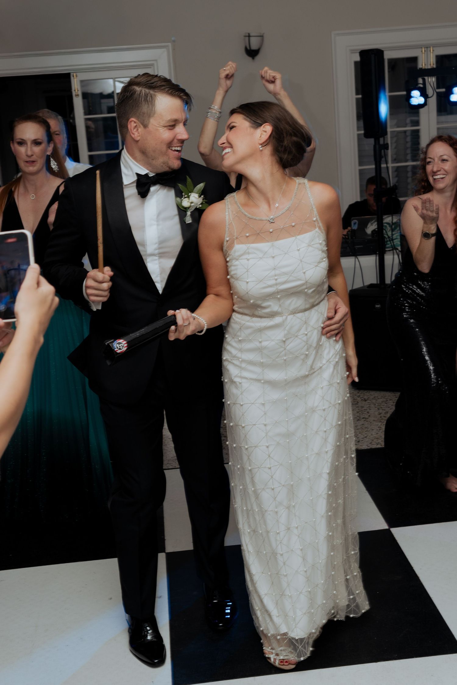 A couple shares a romantic dance at their wedding reception while guests in dark attire look on and smile.