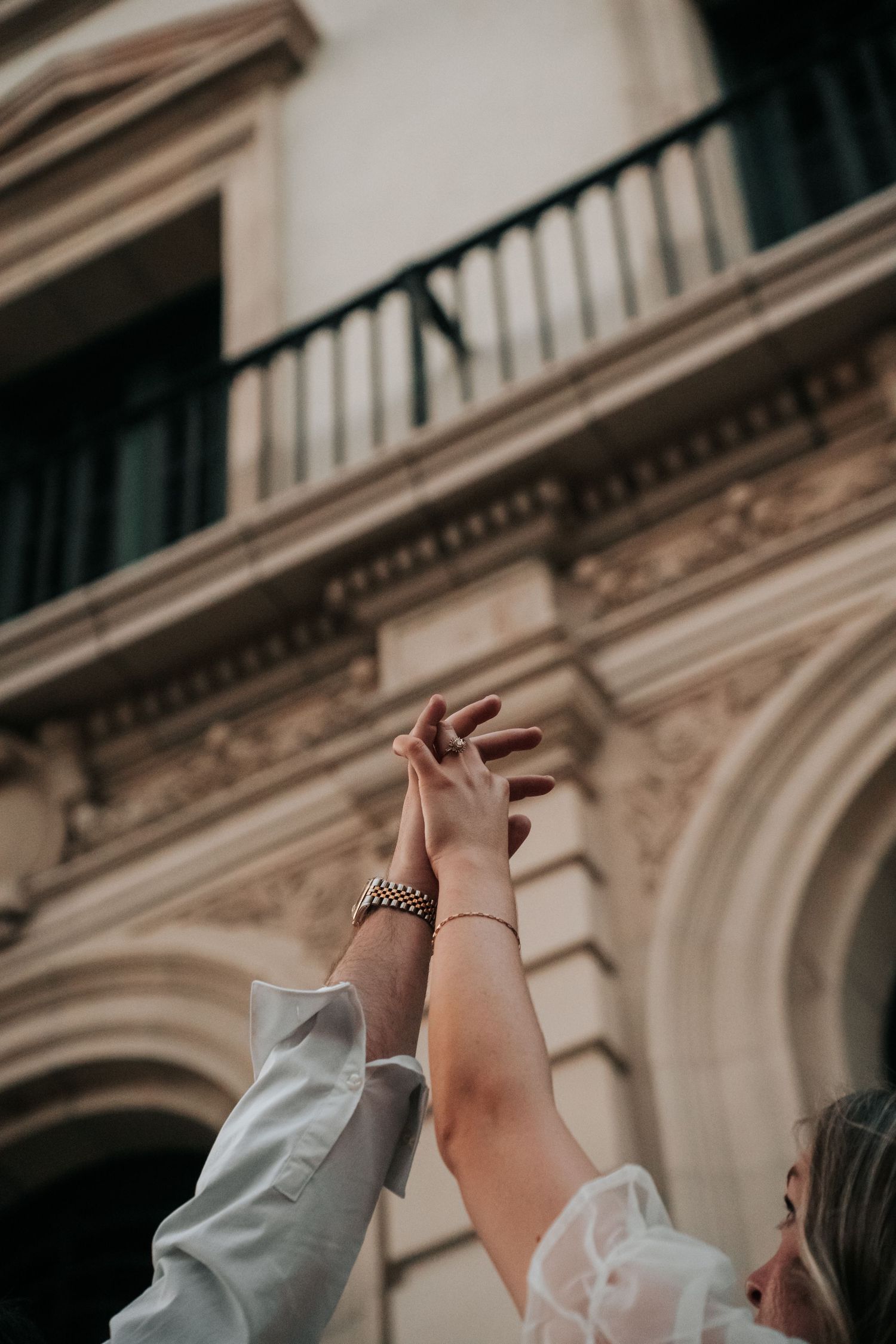 Two raised hands reach upward against an elegant classical building facade with ornate arches and balcony details in downtown Fernandina