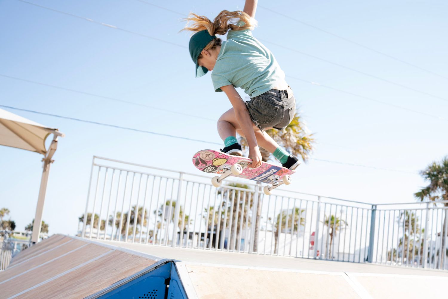 Young skateboarder performing a jump trick at an outdoor skate park on a sunny day.