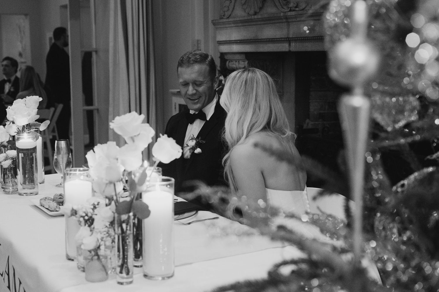 Black and white photo of a wedding reception with guests seated at decorated tables in an elegant venue.