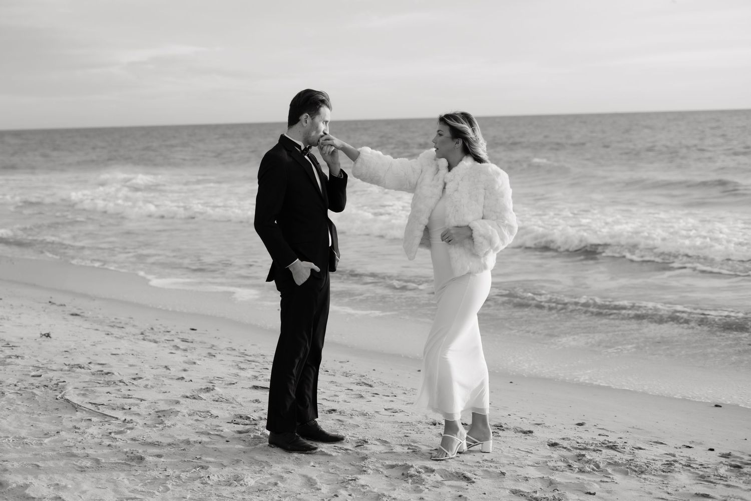A romantic couple walks along a beach shore in black and white photography.