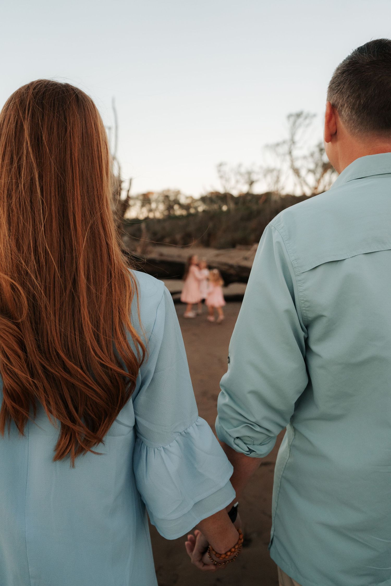 Couple holding hands on beach at sunset wearing coordinating blue outfits.