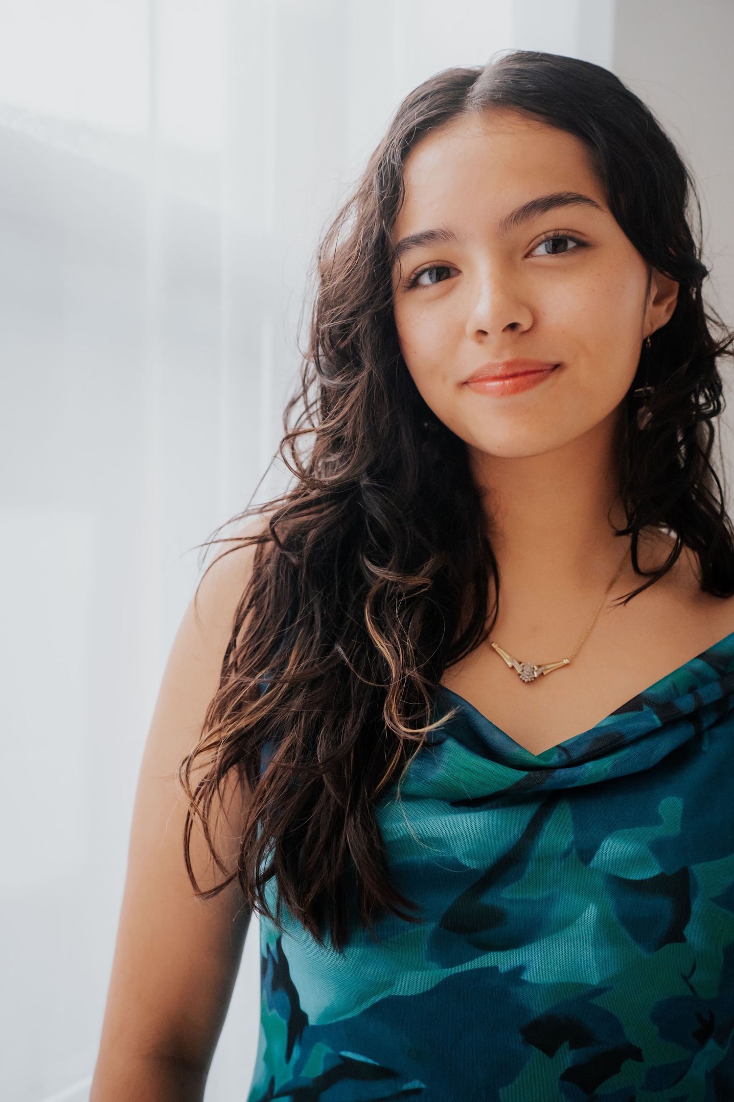 Senior Portrait in teal camo top with flowing dark hair against light background at Luxury Point Studio in Jacksonville, FL