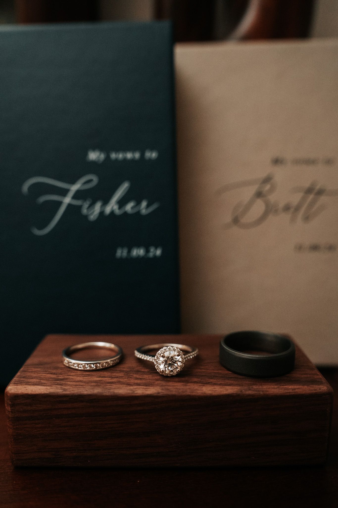 Wedding rings and engagement ring displayed on dark wooden surface with elegant black decor in background.