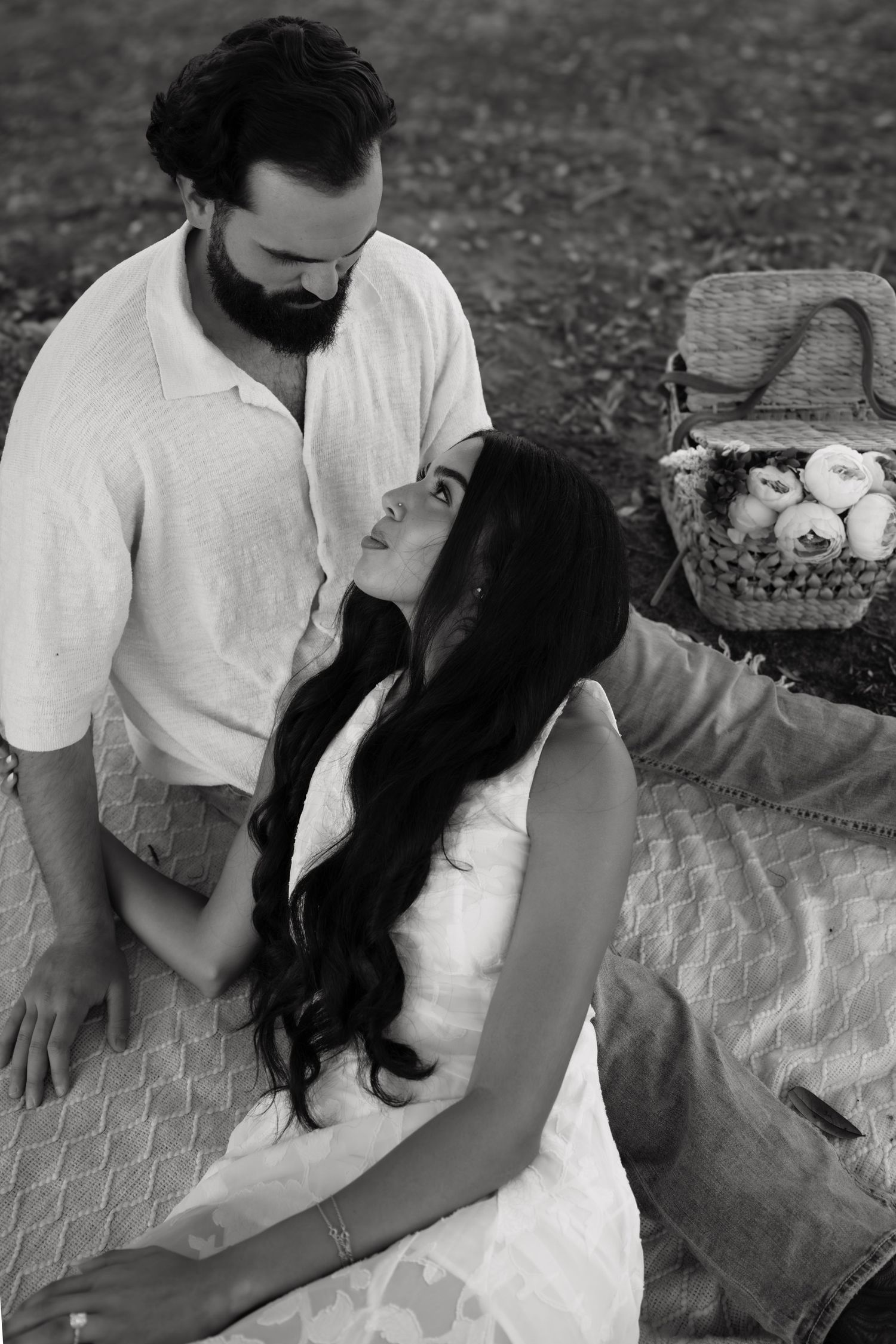 A couple sits together on a blanket having a romantic outdoor picnic on a sunny day.