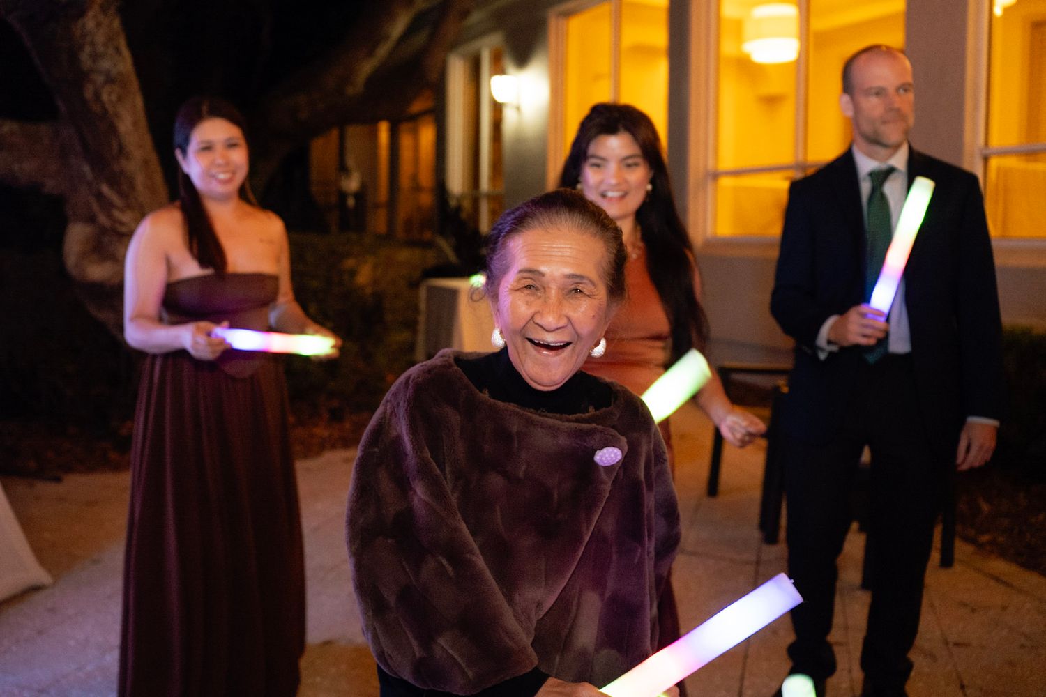Wedding party members hold candles during an evening outdoor ceremony in formal attire.