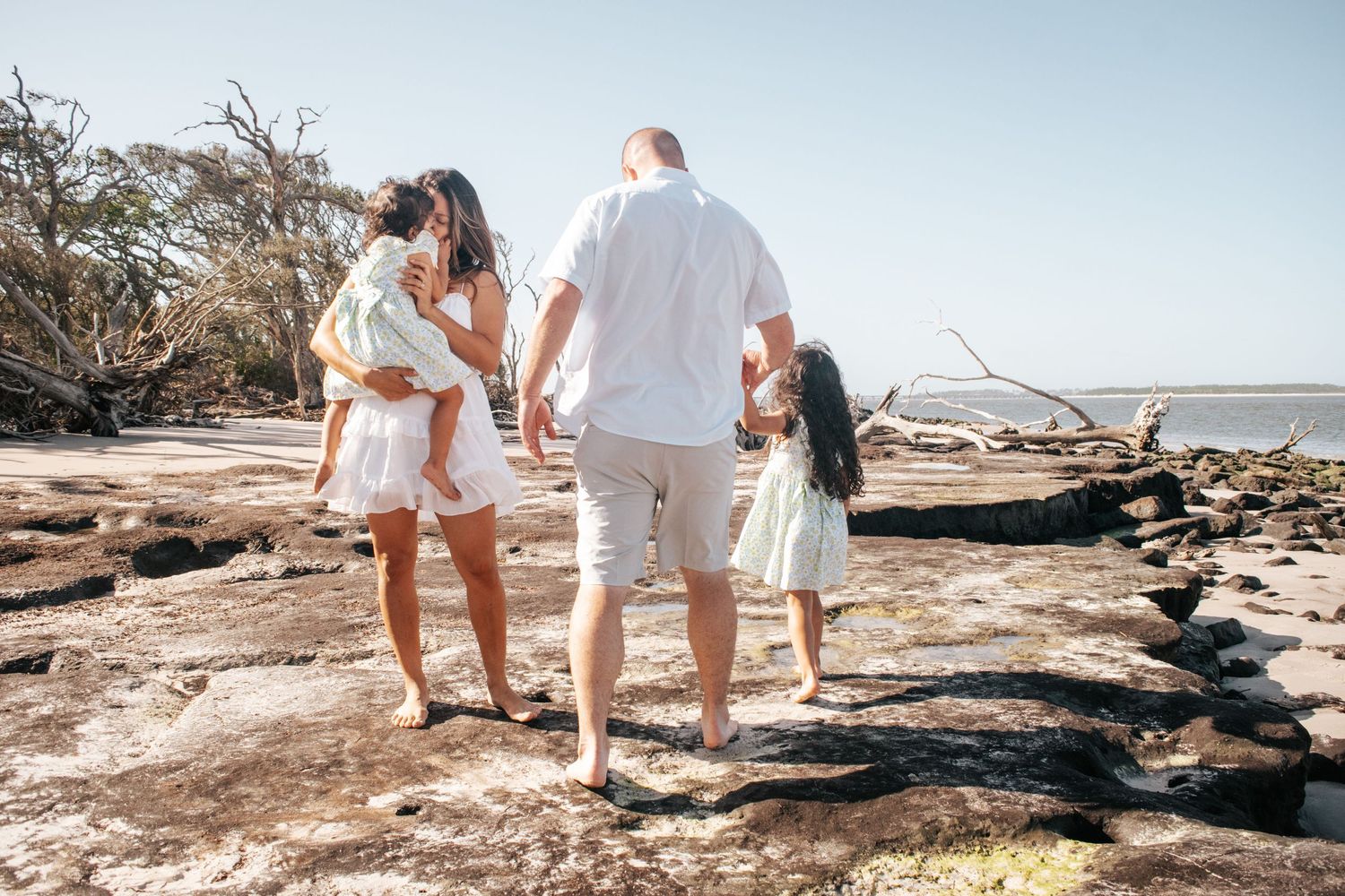 Family walks hand in hand along a rocky beach path.