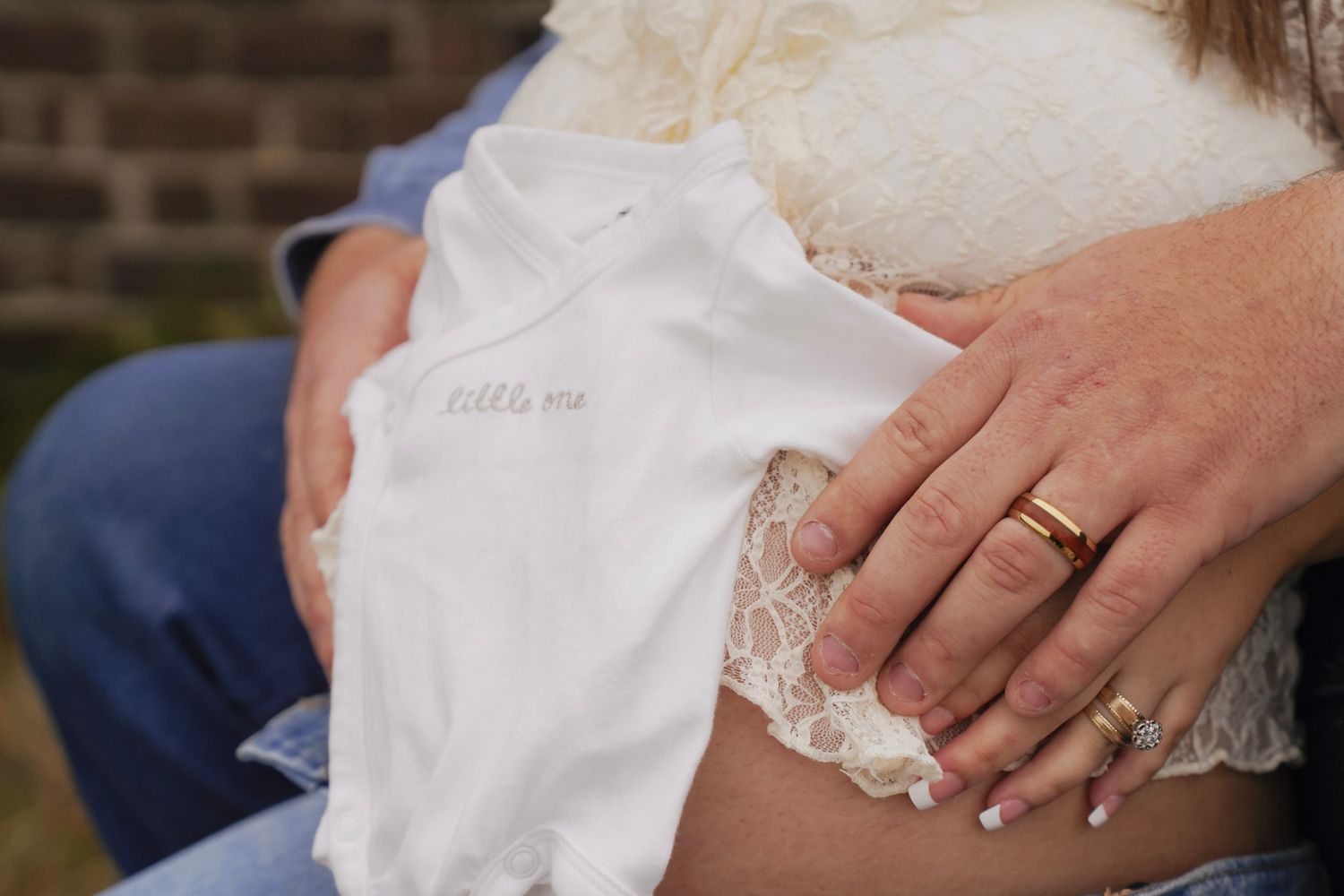 Hands holding a delicate white lace handkerchief with intricate embroidered details and scalloped edges.