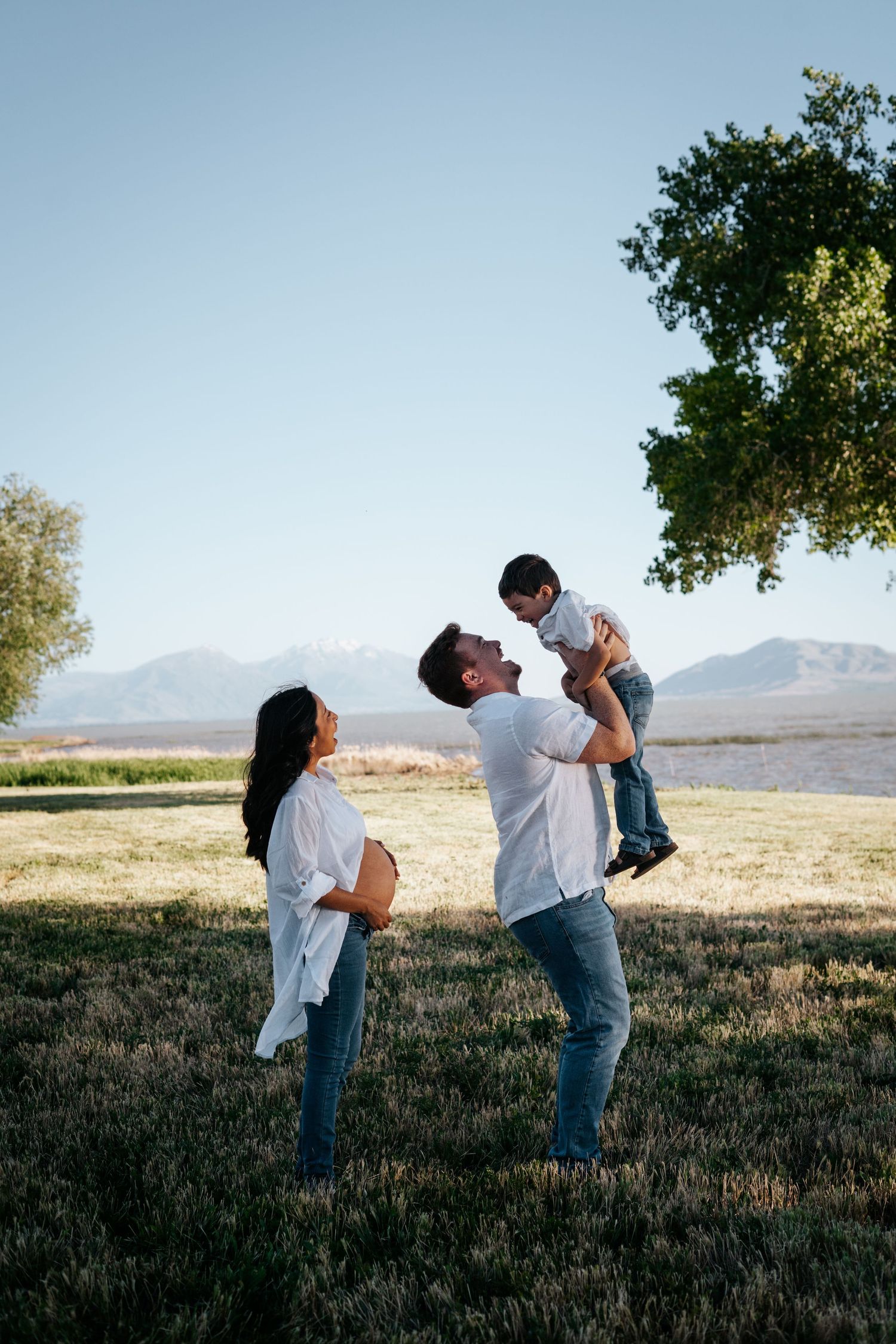 A couple shares a tender moment in a field with mountains in the background at sunset.