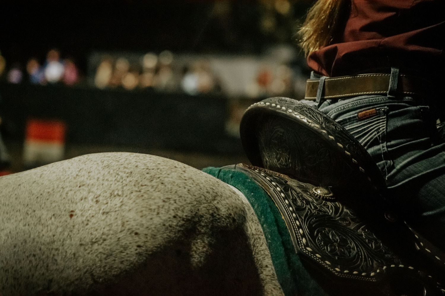 Close-up of a cowboy boot resting on a horse's back during a western riding event.