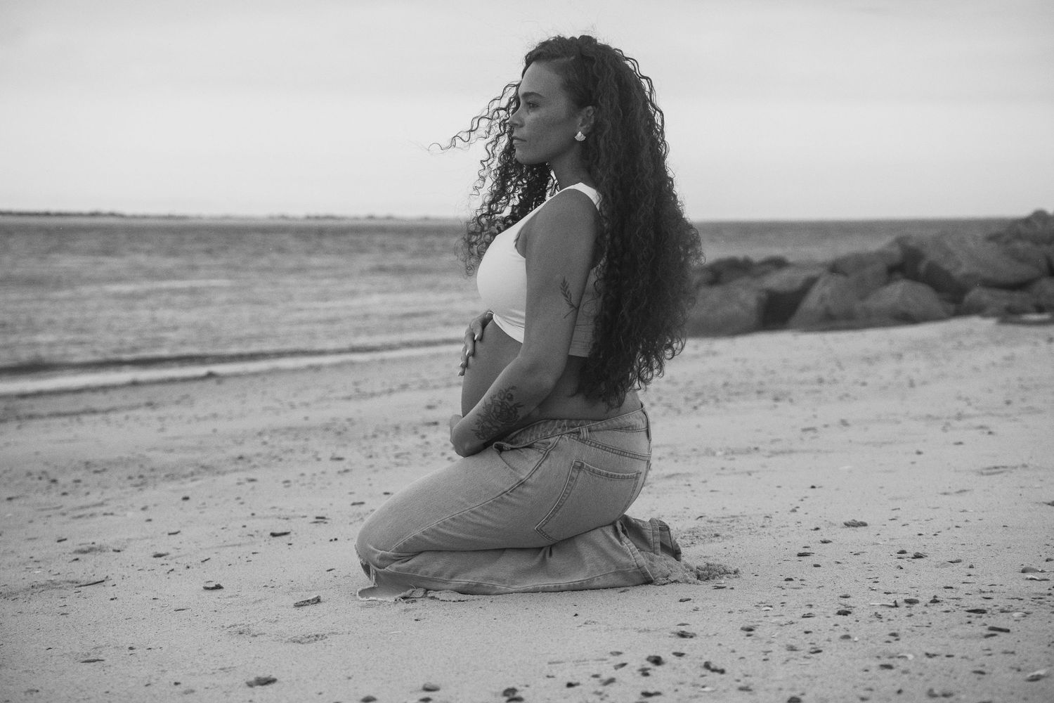 Black and white photo of woman kneeling contemplatively on beach.