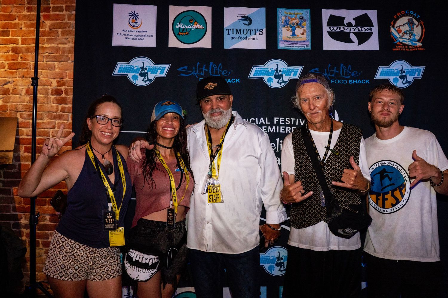 Five people posing together at an official festival premiere event, wearing medals and casual attire against a banner backdrop.
