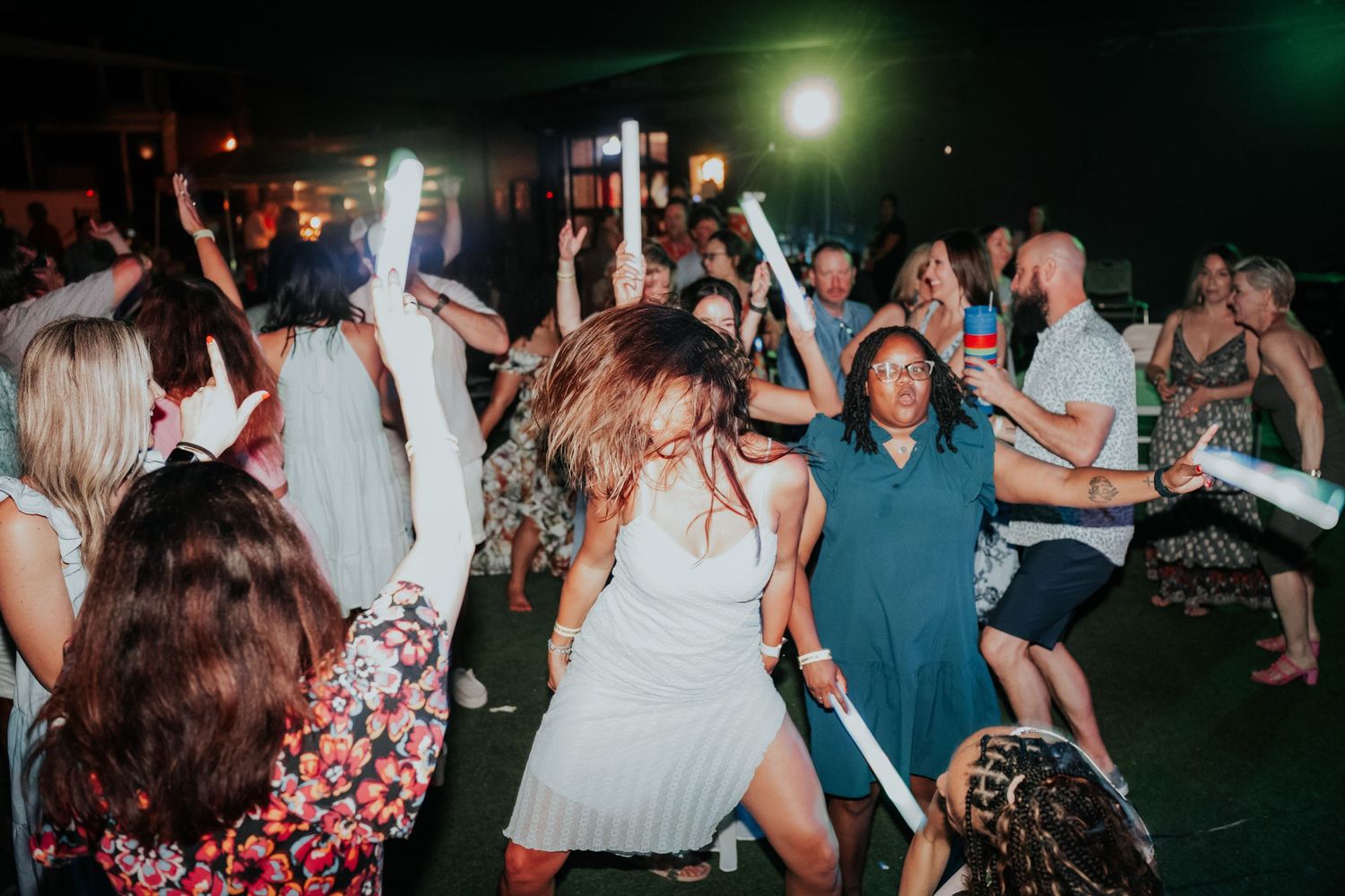 Guests dancing and celebrating at a lively nighttime party event with glow sticks and colorful lighting.