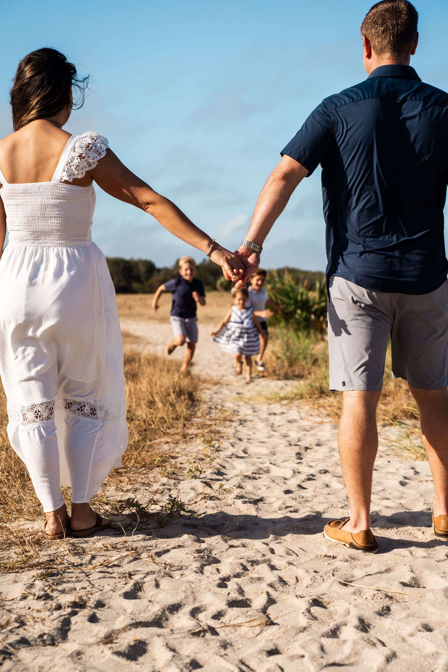Couple holding hands while children run ahead on sandy beach path.