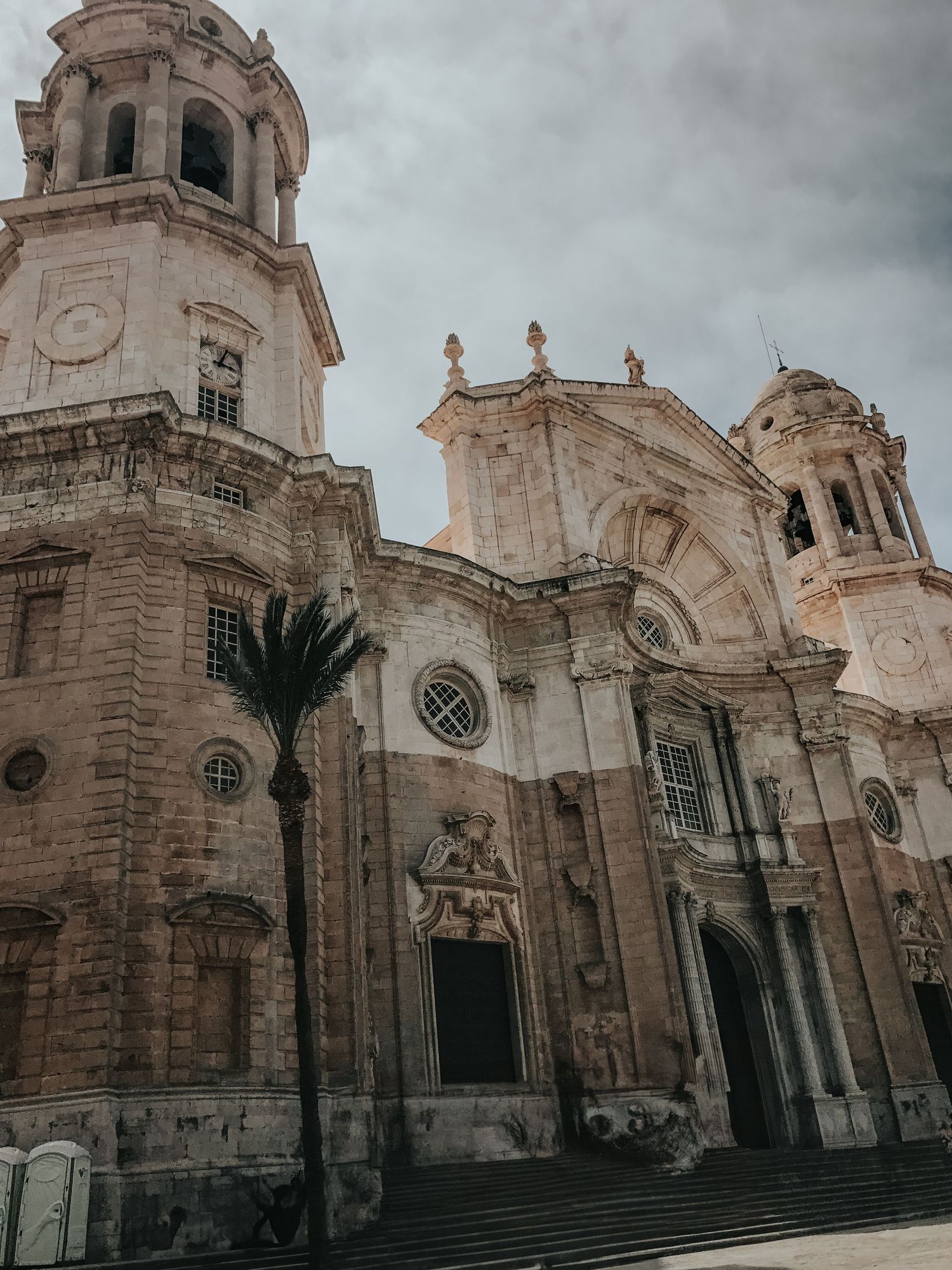 Gothic cathedral facade with twin bell towers and ornate stone architecture photographed under moody cloudy skies.