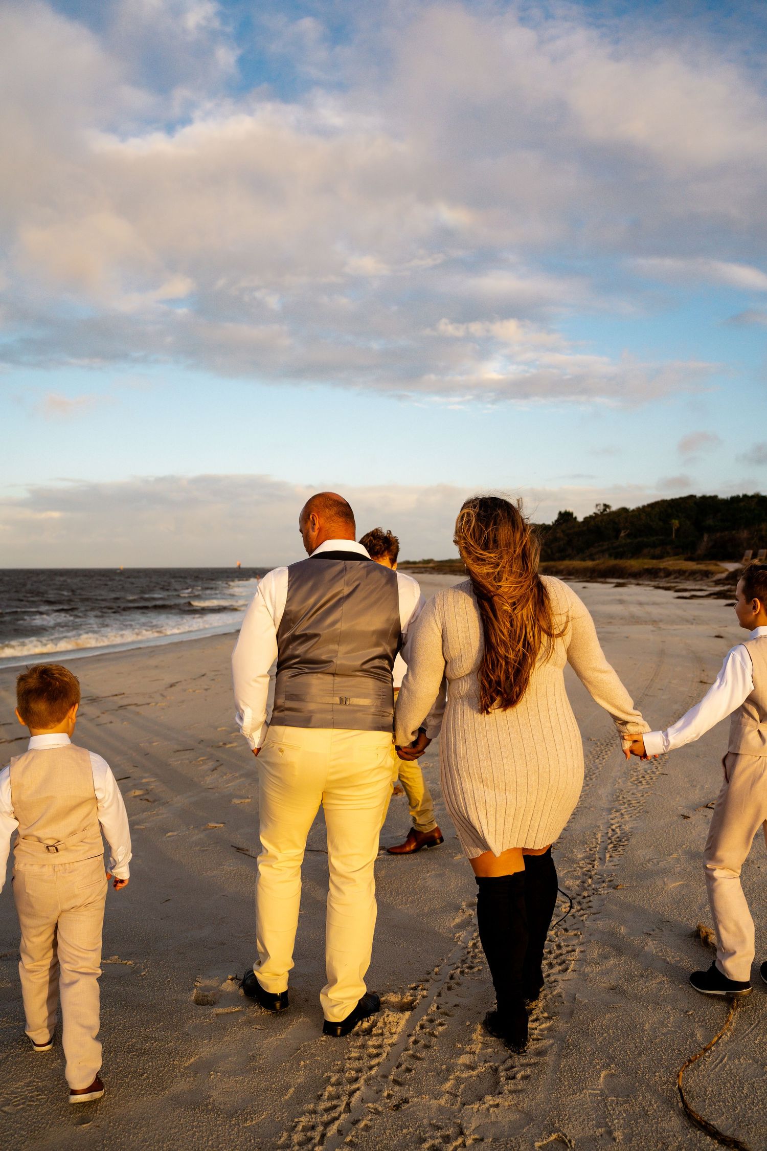 Family walking together on beach at sunset wearing coordinated neutral outfits.