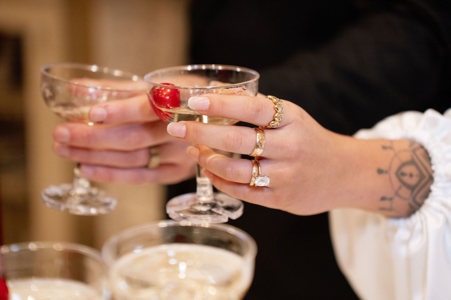 Two hands with rings and tattoos clink champagne glasses garnished with raspberries during a celebration.