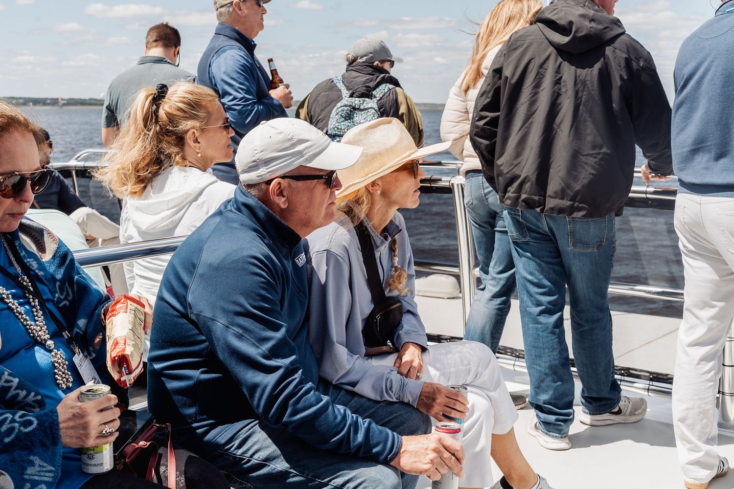 Group of guests enjoying a sunny boat cruise on the water, seated and standing on deck.