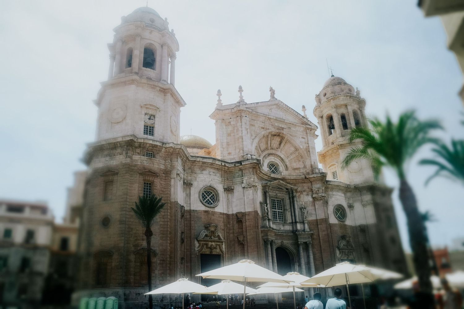 Exterior view of Cadiz Cathedral in Spain with ornate Baroque architecture and white umbrellas in the foreground.