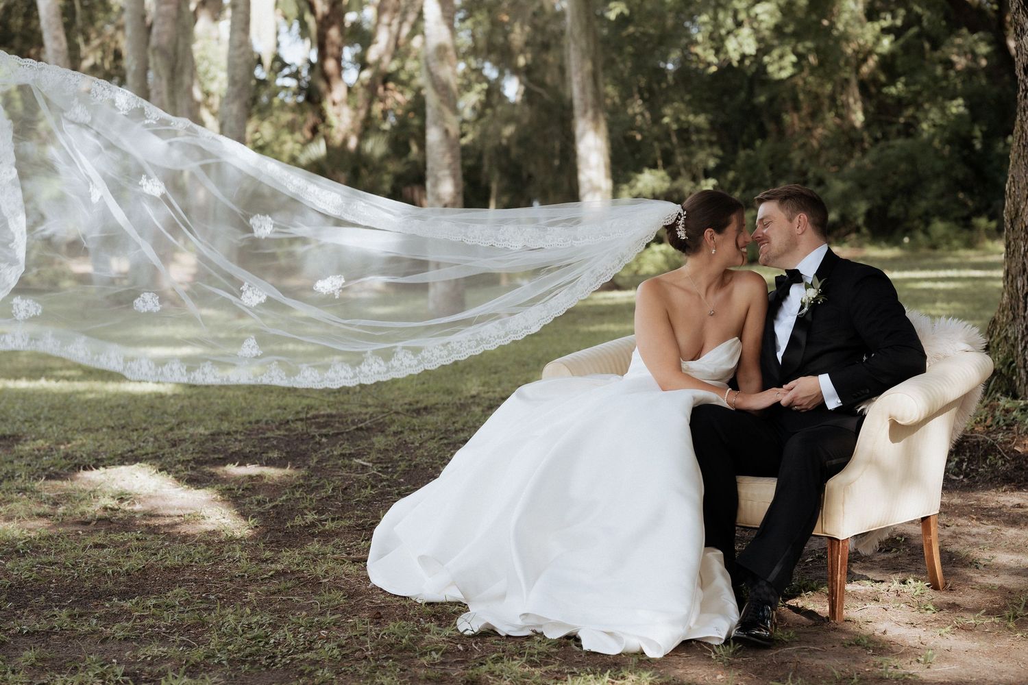 A romantic wedding couple shares intimate moments in a sunlit garden setting with flowing white dress and veil details.