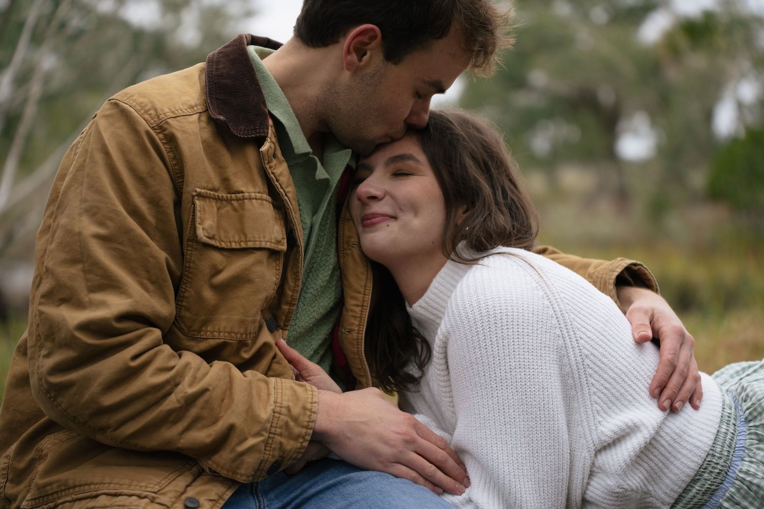Couple in brown jackets share tender moments outdoors during an autumn photoshoot in nature.