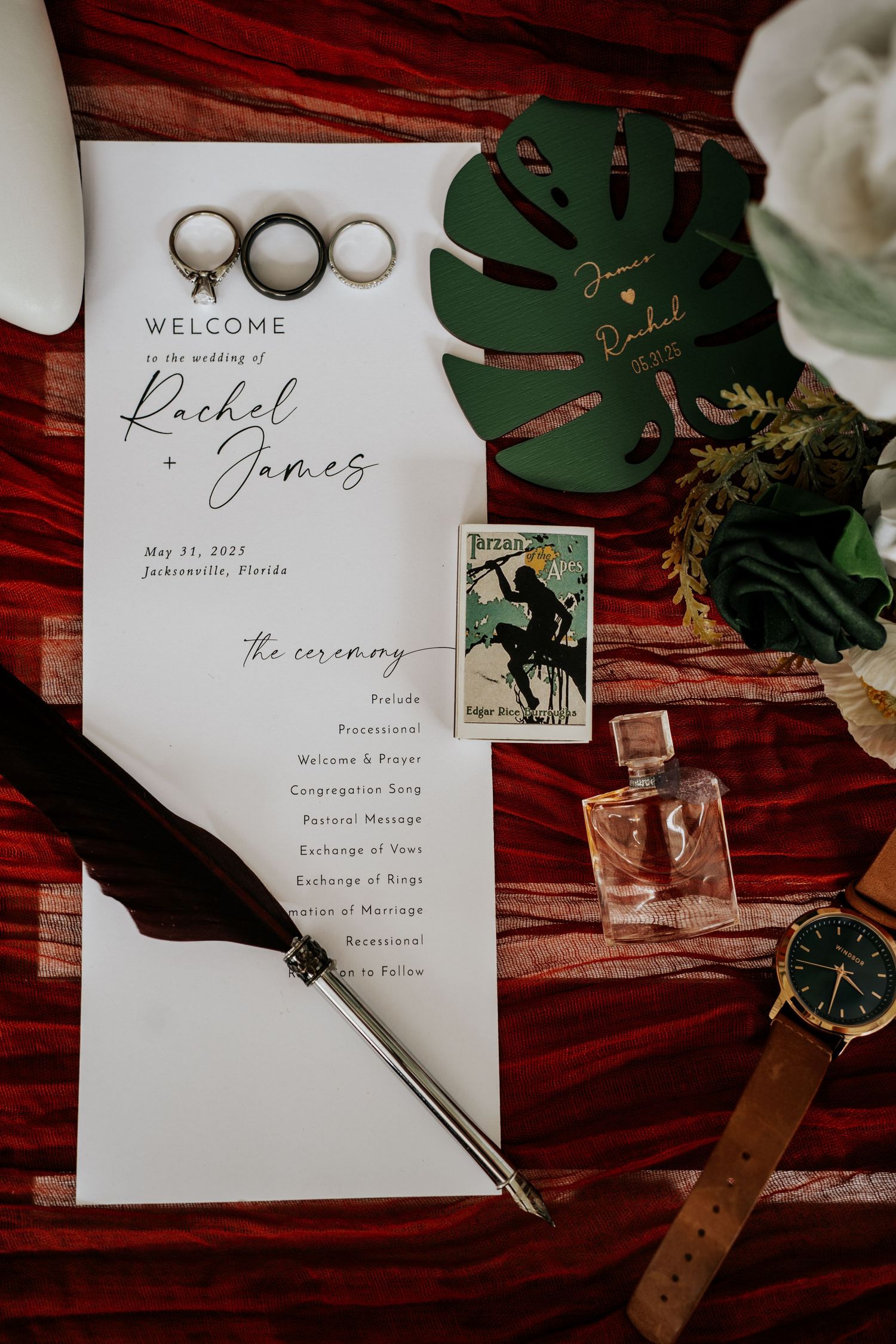 Elegant wedding invitation suite with calligraphy on white paper displayed with greenery and vintage keys on dark wood surface.