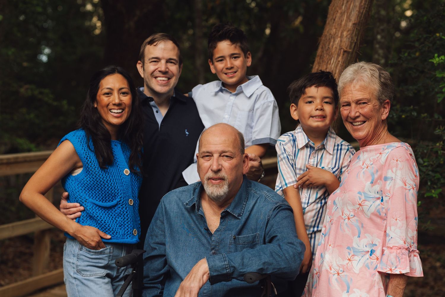A family poses together outdoors in coordinated outfits of blue and pink tones for a portrait session.