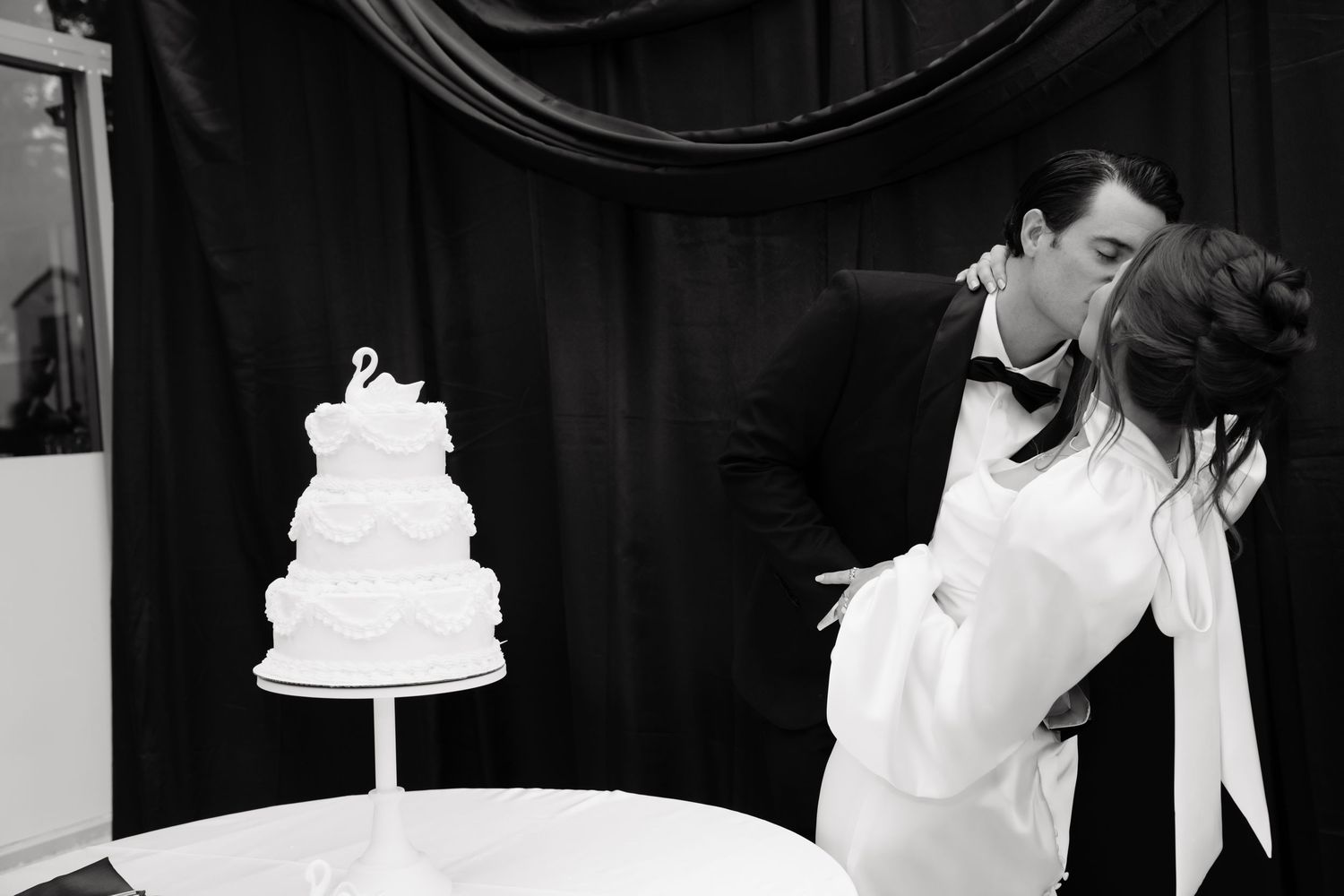 A romantic black and white wedding photo with a traditional white tiered cake in the foreground.