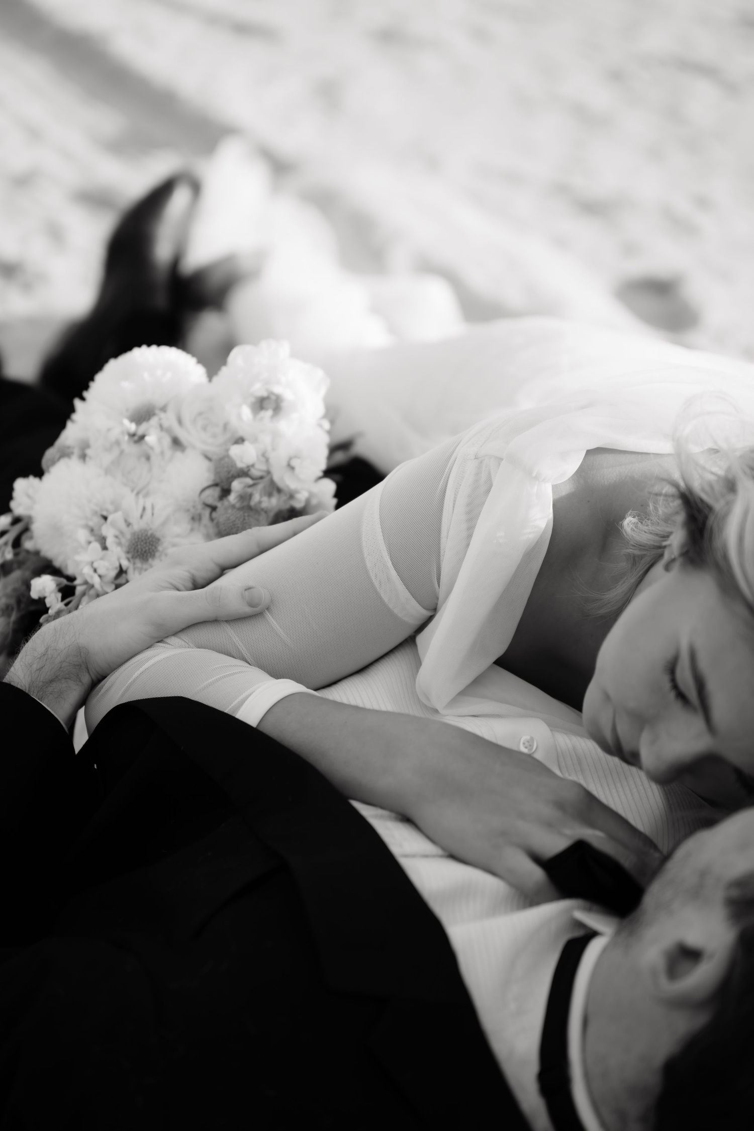 A black and white wedding photo showing a tender moment with flowers and formal attire.