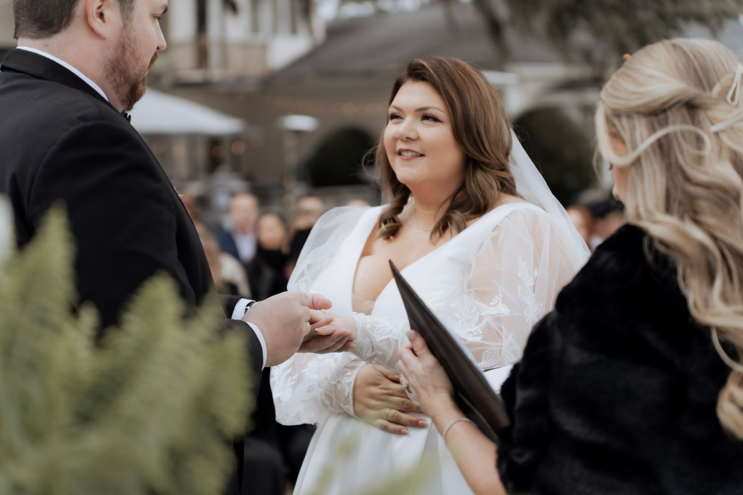 A wedding couple and guests share laughter and drinks during an outdoor celebration reception.