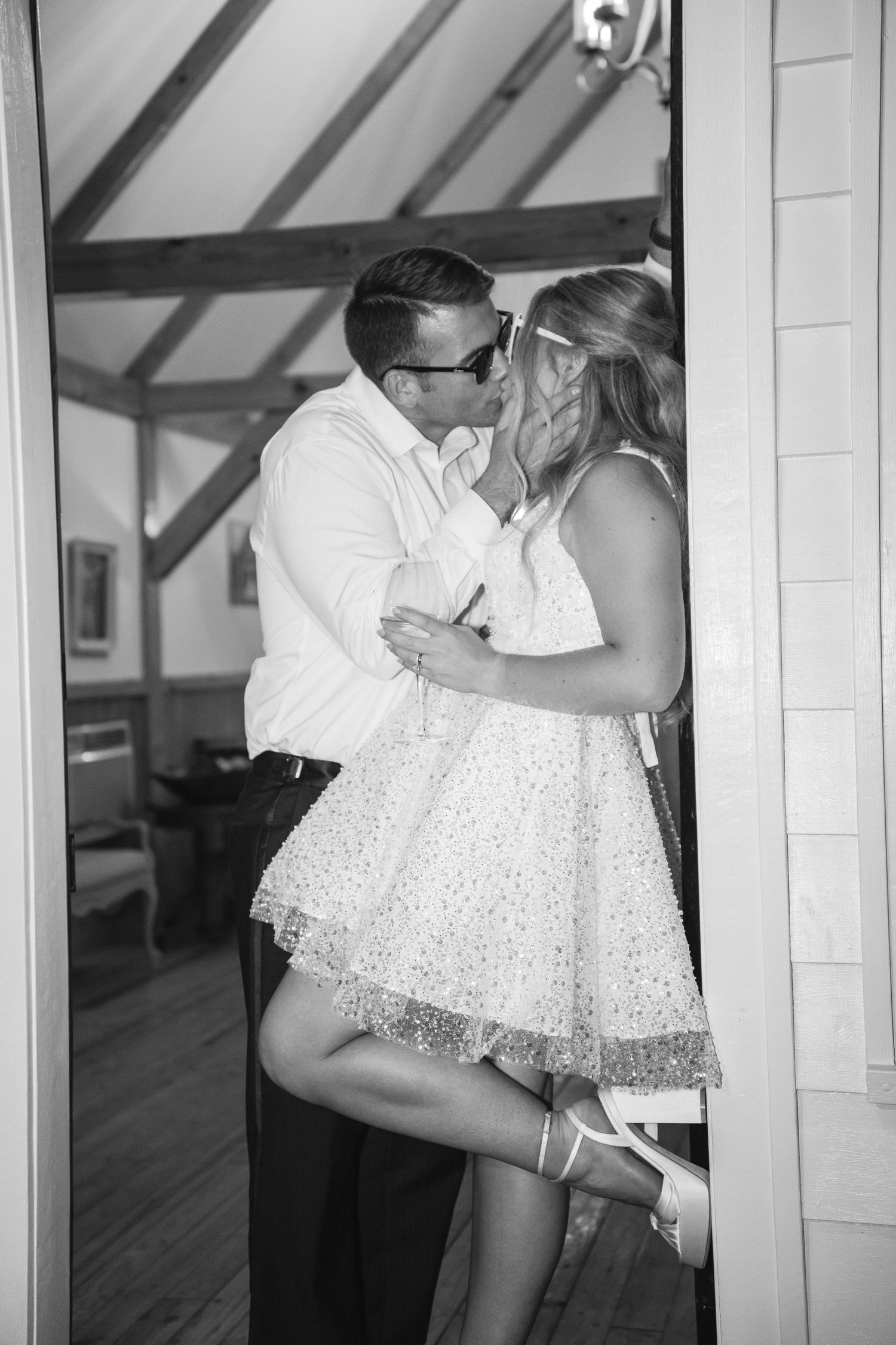 A black and white wedding photo showing a couple sharing an intimate kiss in a rustic indoor setting.