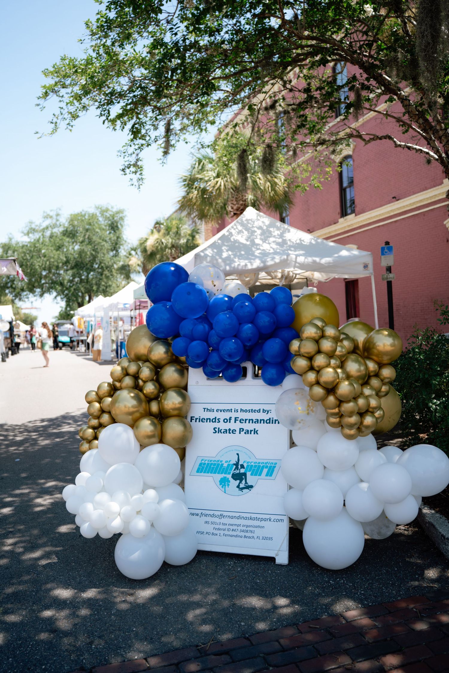 Blue, gold, and white balloon arch display for Friends of Fernandina Skate Park event at outdoor festival.