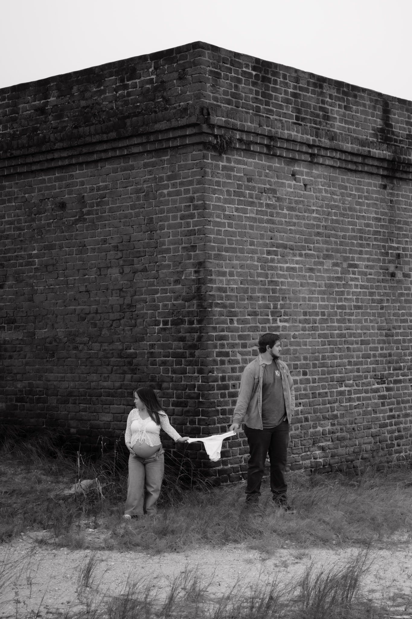 Black and white sequence of three figures walking and crouching behind a brick wall in an artistic composition.