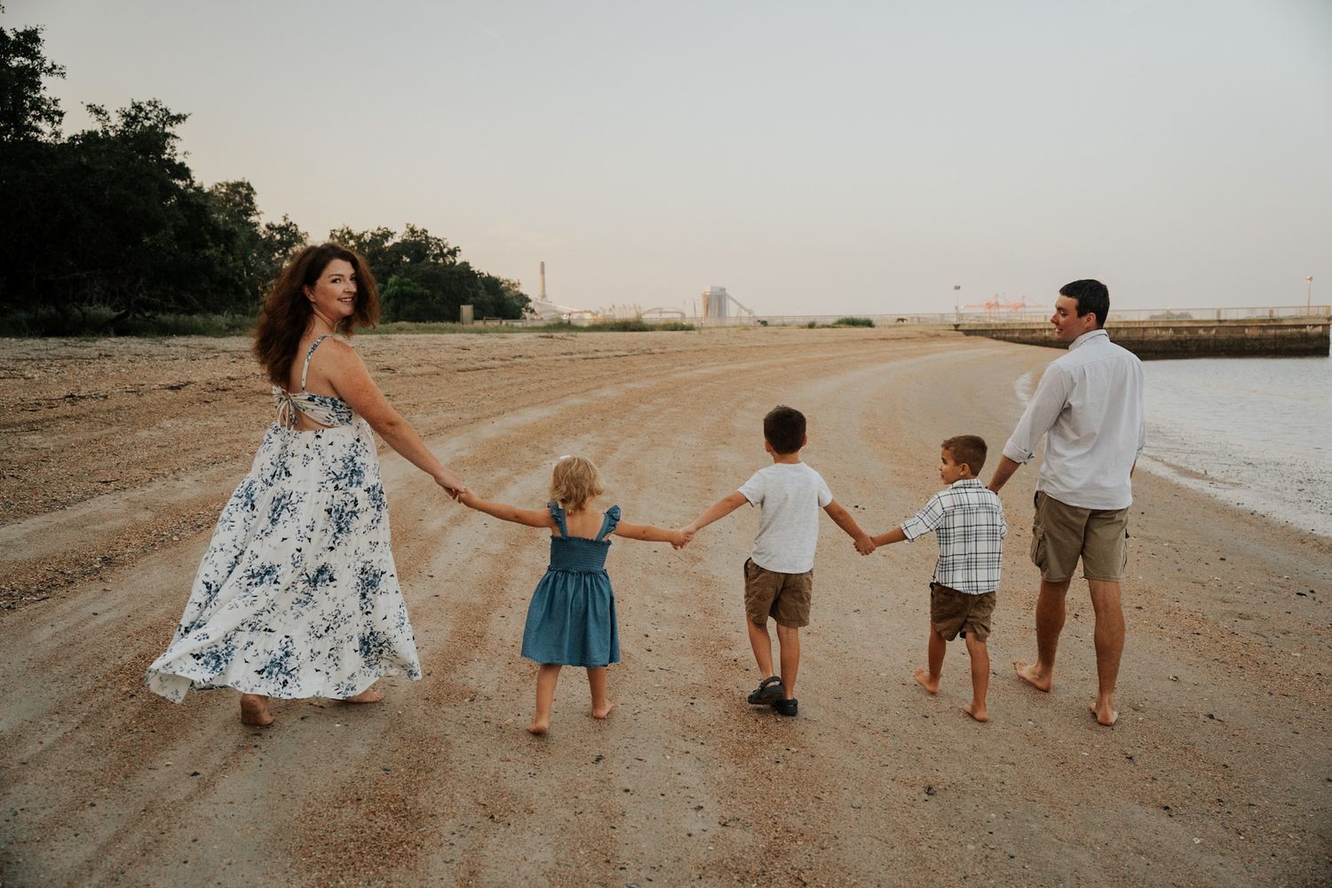 Family holding hands walking along sandy path with floral dress and casual summer outfits.