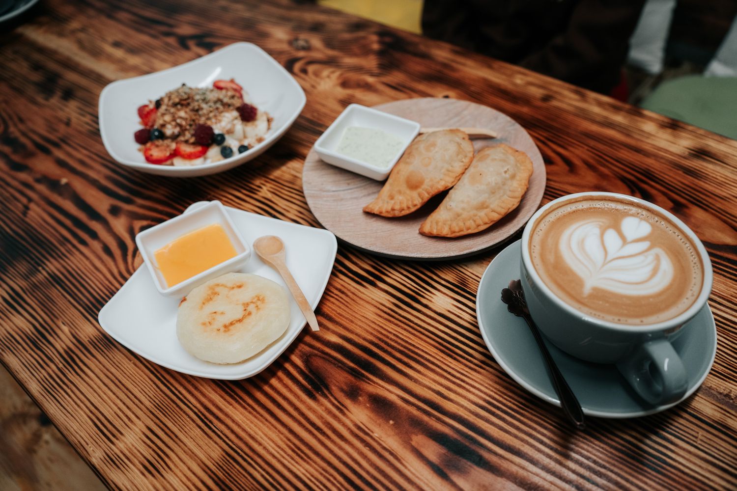A rustic breakfast spread on wooden table with latte art coffee, toast, butter, and a side salad.